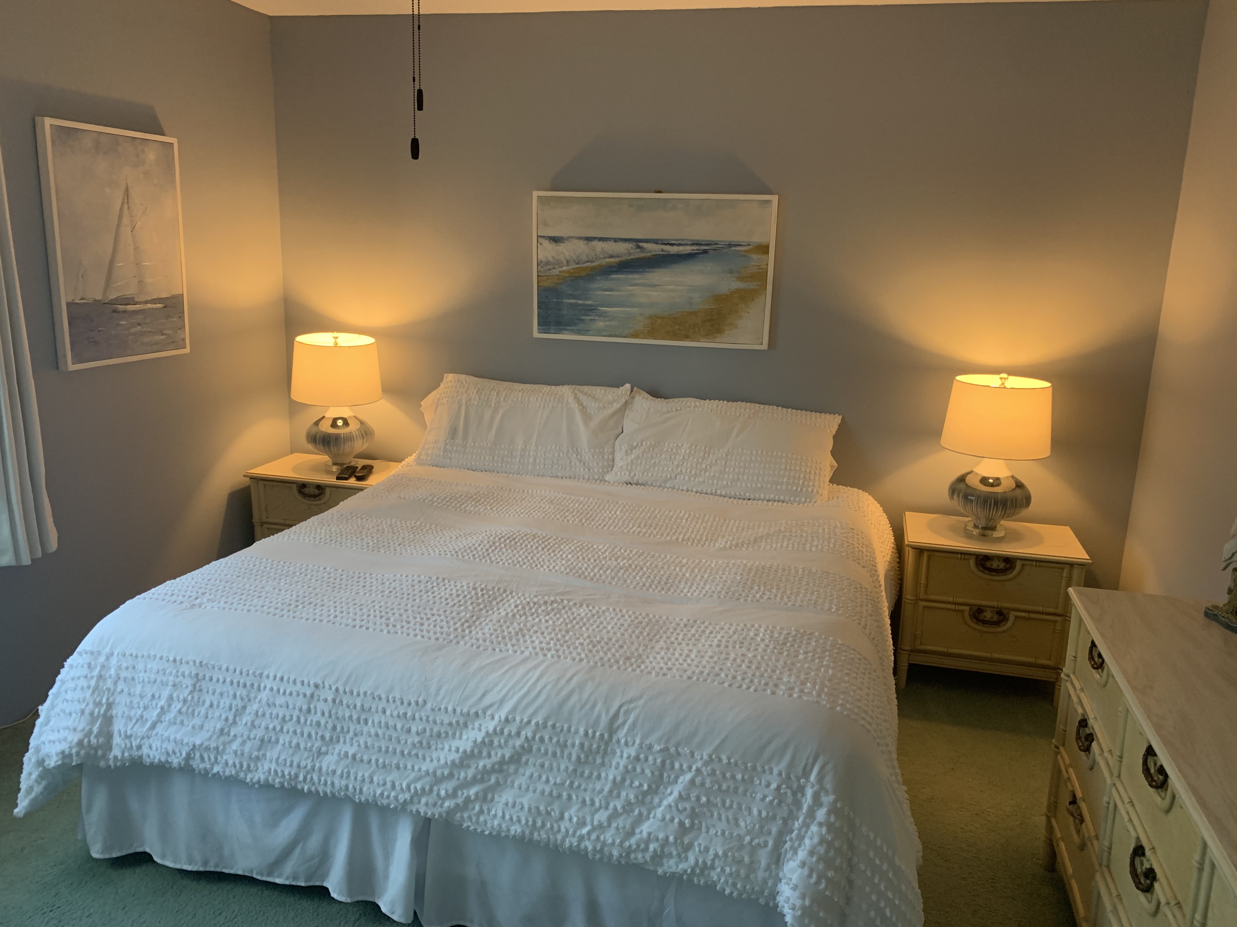 Primary bedroom with white bedding, lamps, and coastal art